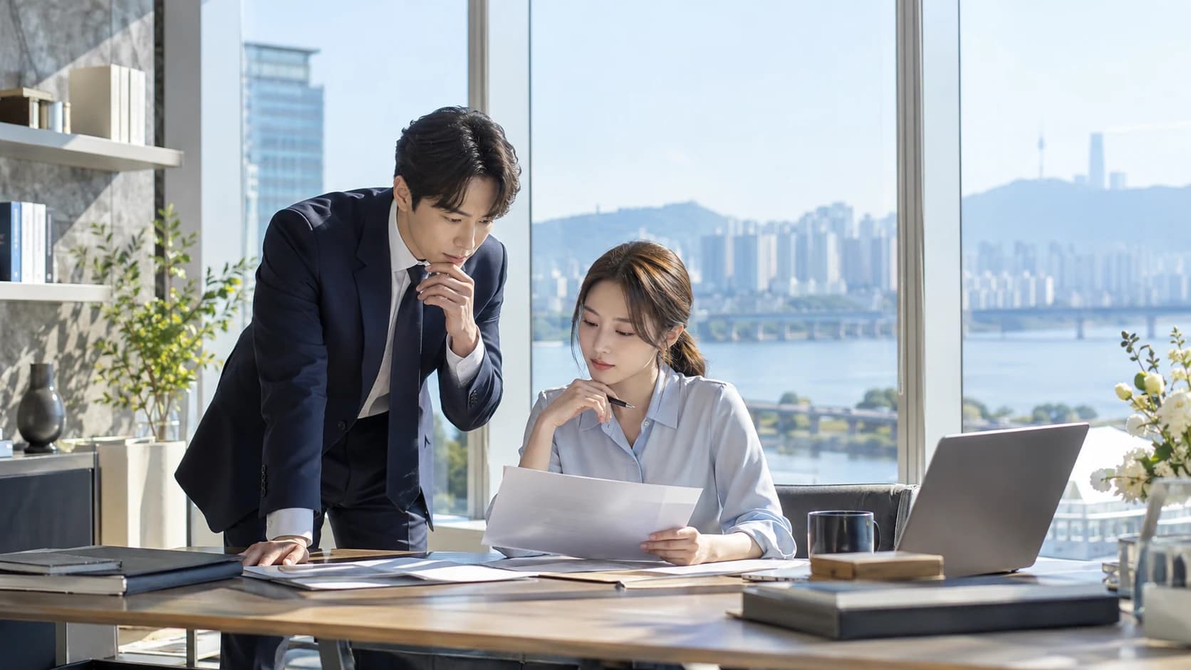 밝은 사무실에서 두 사람이 문서와 노트북을 함께 검토하는 장면